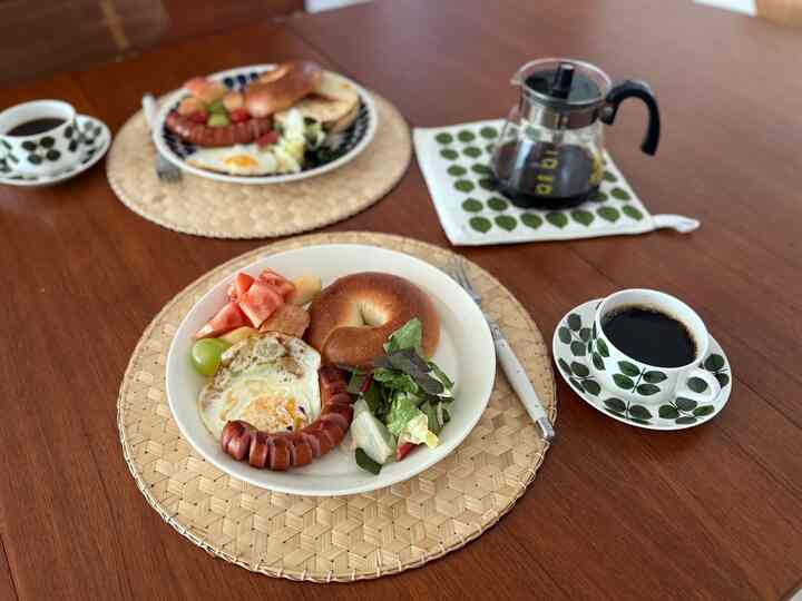 茶色の木目調ダイニングテーブルに丸い竹製マットと白い皿、コーヒーカップが配置された雰囲気のあるホームブランチ空間