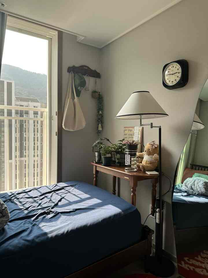 ブルーの寝具とブラウンウッド家具が調和したナチュラルな6畳の寝室、窓越しの景色と植物が配置された温かみのある空間