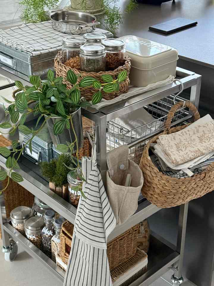 ナチュラルな色調のキッチン、ステンレスのキッチンワゴンに収納バスケットやキッチン用品が整然と配置された印象的な空間