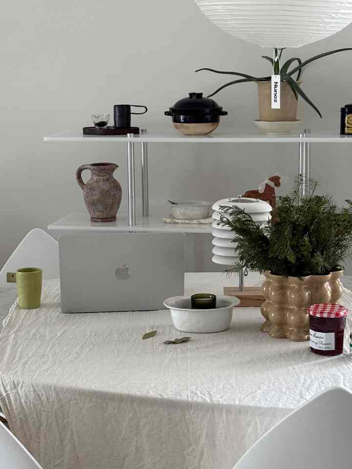 ナチュラルカラーとホワイトトーンのリビング、ダイニングテーブルとテーブルクロス、ペンダントライト、植物が配置された温かみのある空間