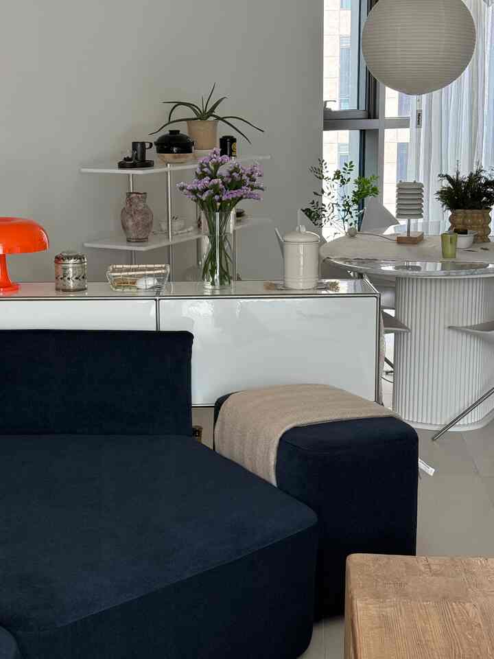 白とネイビートーンが特徴的なリビング兼ダイニングスペース、花瓶のある棚、ソファ、丸いダイニングテーブルが配置された自然な雰囲気のインテリア