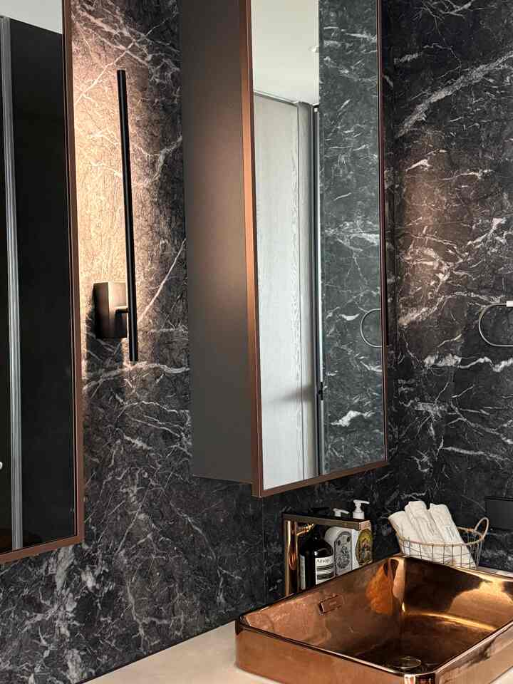 黒い大理石の壁とゴールドの金属製洗面台があるモダンなトイレのパウダールーム