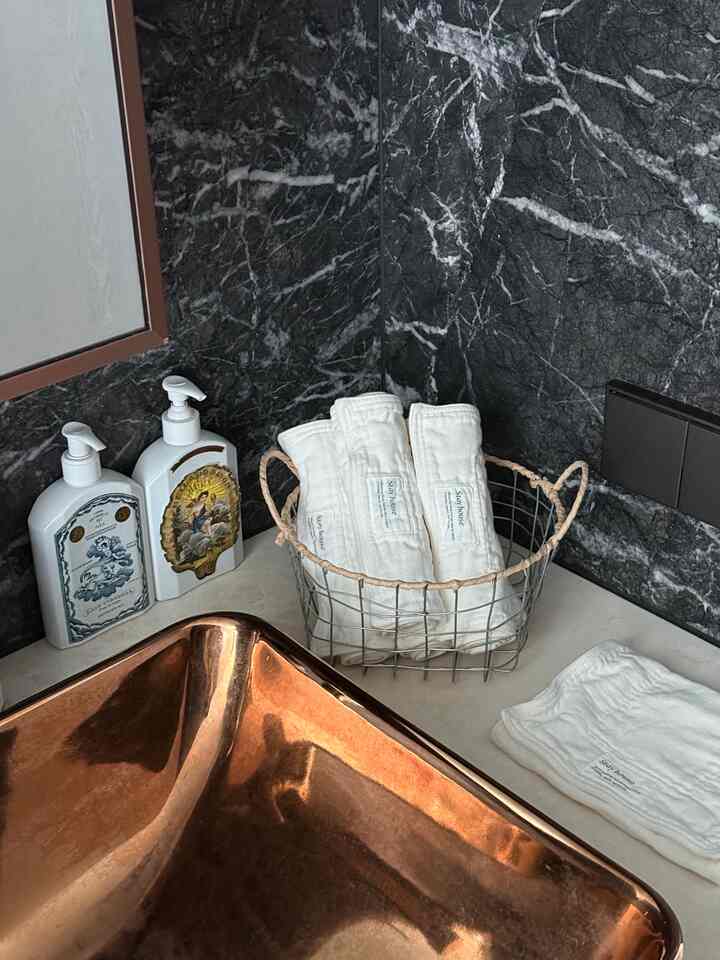 ゴールドの洗面台と白いタオルが配置された黒い大理石の壁面の雰囲気のあるバスルーム