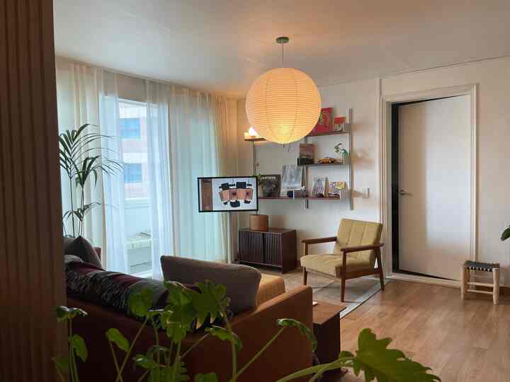 明るいナチュラルモダンのリビング、マスタードイエローのアームチェアと木目調家具、大きな丸いペンダントライトが配置された温かみのある空間