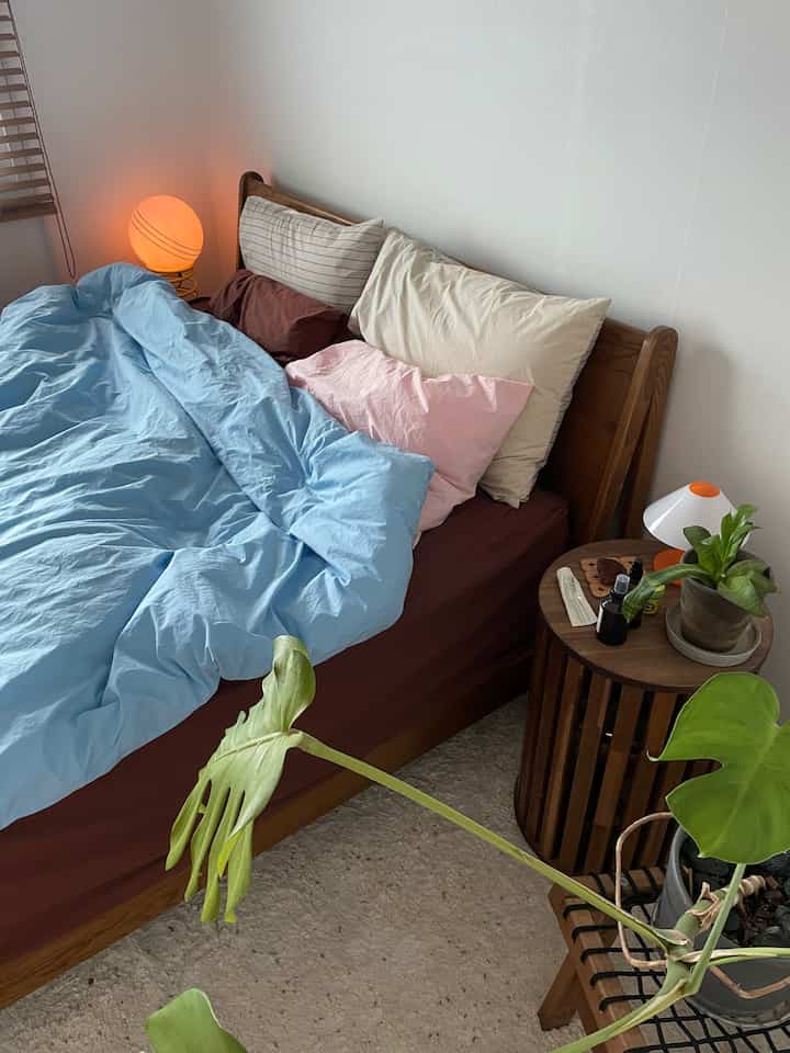 ナチュラルで木目調の寝室、枕とパステルトーンの掛け布団カバーが配置された雰囲気のあるインテリア