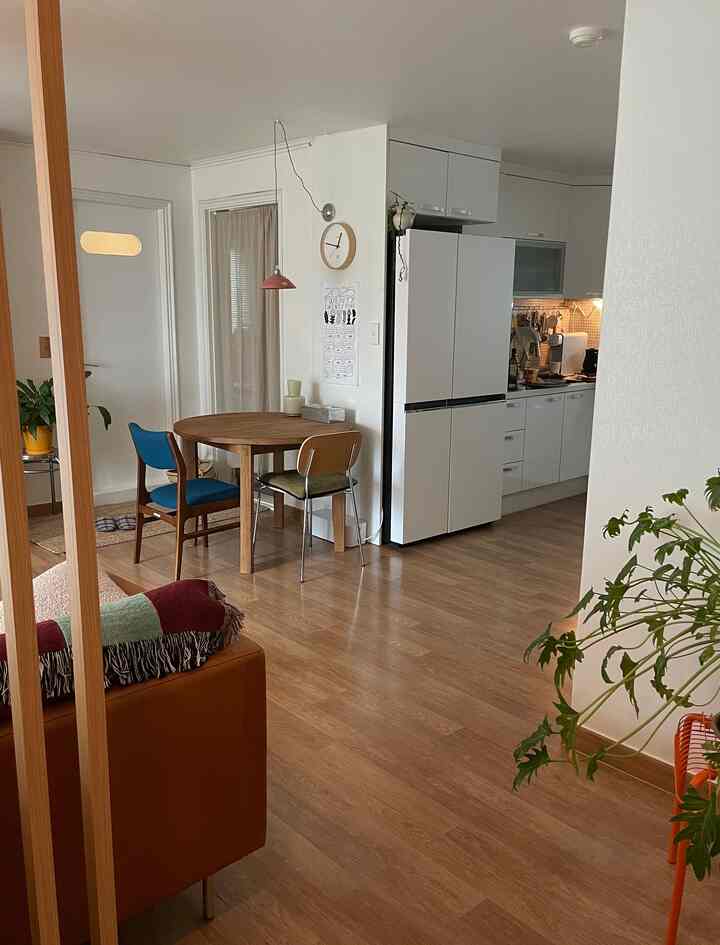 白い壁と木目調の床が調和するモダンなダイニング、丸いダイニングテーブルと椅子が配置された居心地の良いキッチンと玄関スペース