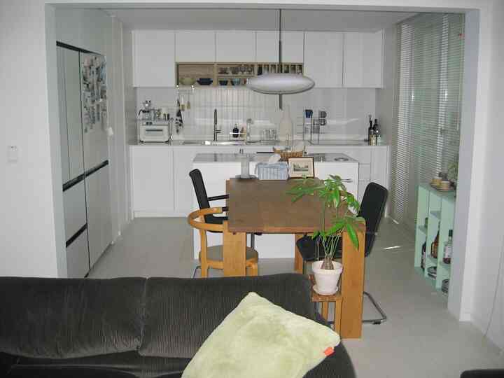 ホワイトとウッドトーンのモダンなリビングとキッチンダイニング、グレーのソファが配置された空間