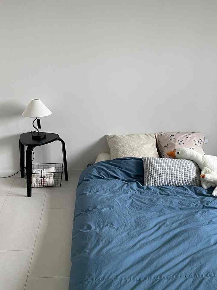 白い壁と床、ブルーの寝具とシンプルな家具が配置された寝室のインテリア