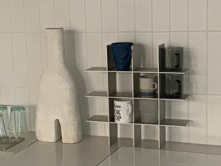 白いタイル壁とステンレス製のカップ棚に様々なカップが置かれたモダンなキッチン