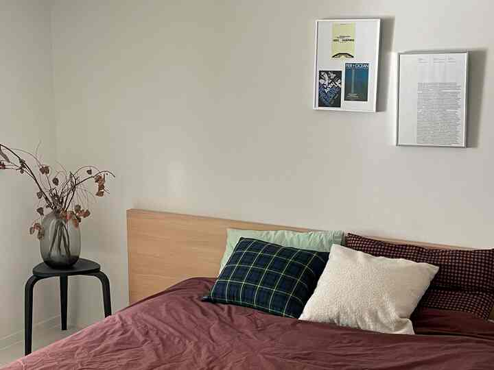 ナチュラルな色調の寝室、木製ベッドにバーガンディの掛け布団カバーと多様なクッションが配置された温かみのある空間