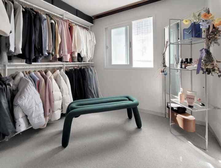 ホワイトとグレーのトーンのウォークインクローゼット、左側のハンガーと中央のグリーンベンチが配されたモダンな収納空間