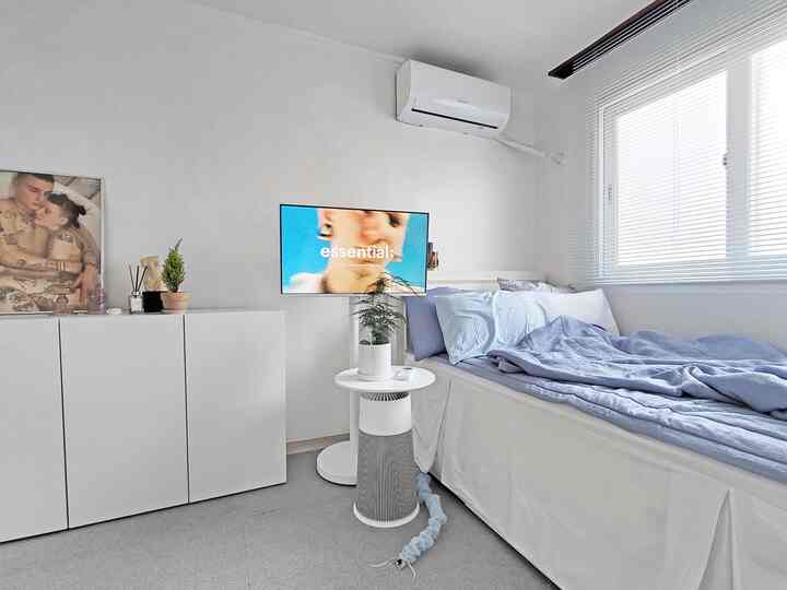 白とライトブルーのトーンが特徴の狭い寝室、ベッドと白いチェストが配置されたシンプルな空間