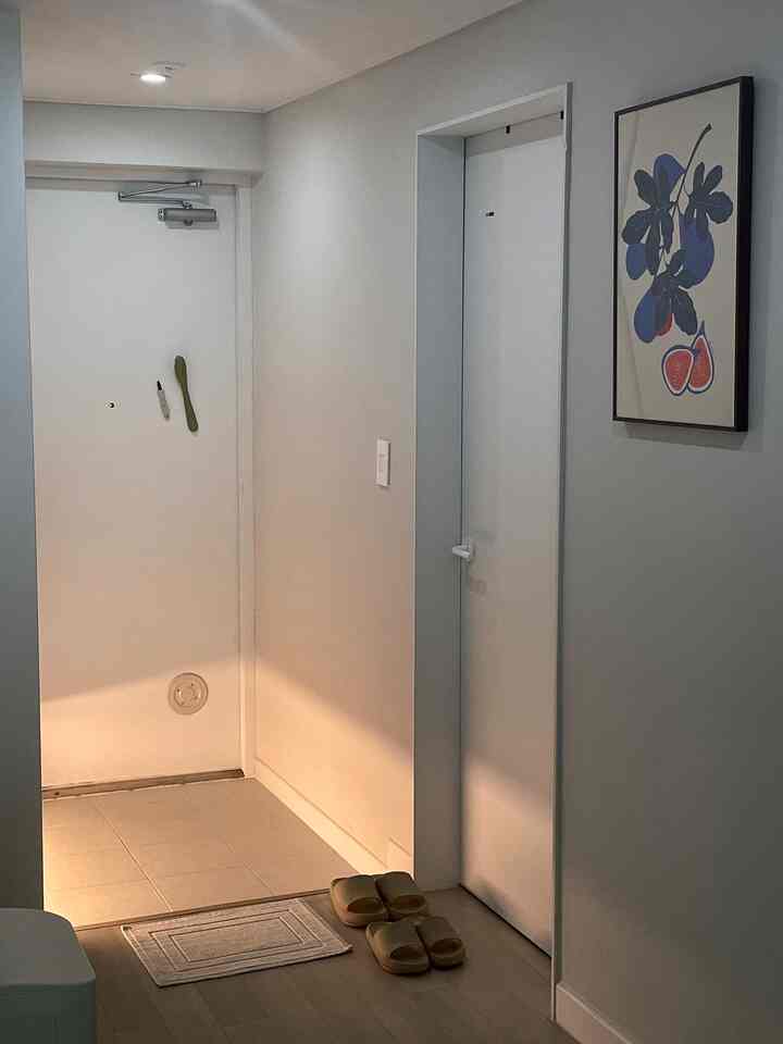 ホワイトと木目調の玄関、壁にポスターが掛けられ、スリッパが床に置かれた雰囲気のある空間