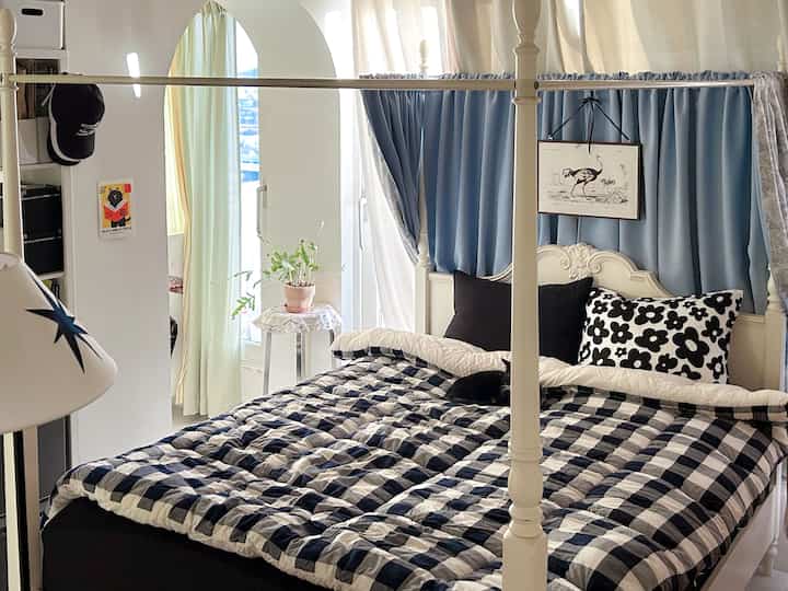 ネイビーとホワイトのチェック寝具とフローラル柄の枕が置かれた寝室、カーテンと猫がいる温かみのある空間