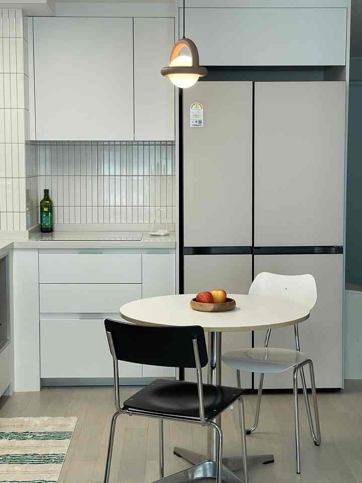 ホワイトとベージュのトーンのコンパクトなキッチン、アゴ バルーン ペンダントライトとダイニングチェアが配置されたモダンな空間
