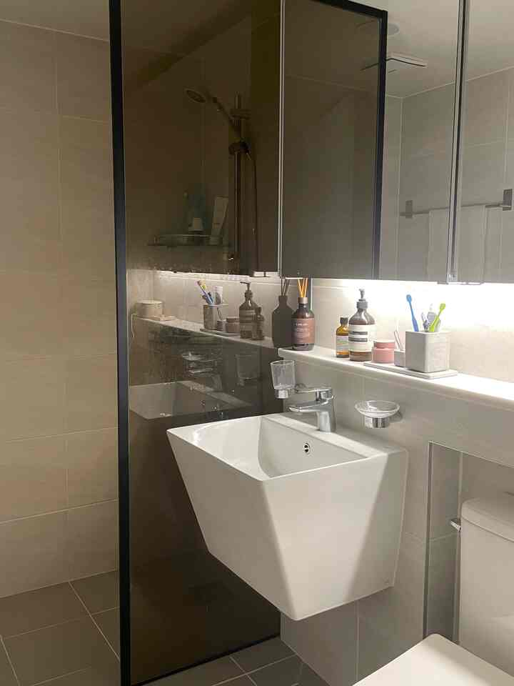 ホワイトとグレーのトーンのバスルーム空間、鏡の下にセンサー間接照明があり、洗面台とバスルーム用品が配置された清潔感のあるインテリア