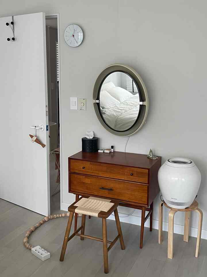ナチュラルな色調のワンルームの化粧台スペース、木製の化粧台とスツール、丸い鏡と白い加湿器が配置された清潔感のあるインテリア