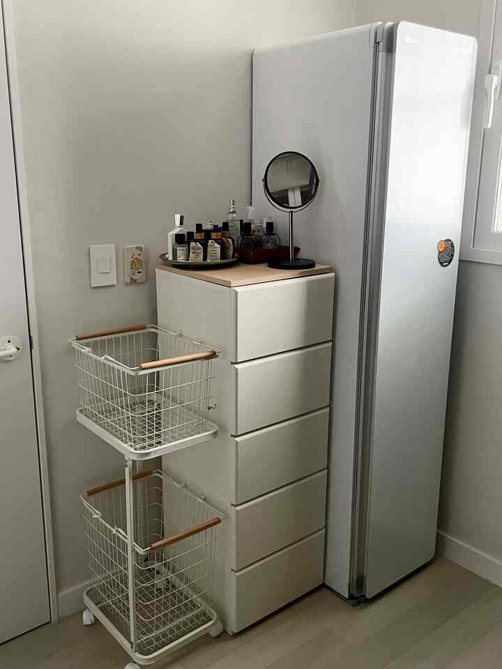 暖かみのあるベージュとホワイトのトーンのウォークインクローゼットの一角に、キャビネット、スタイラー、ランドリーバスケットが整頓された実用的な空間