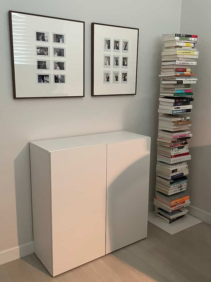 ホワイトトーンの壁と床、シンプルな収納キャビネット、本棚、ポラロイドフレームが配置された清潔感のあるリビングスペース