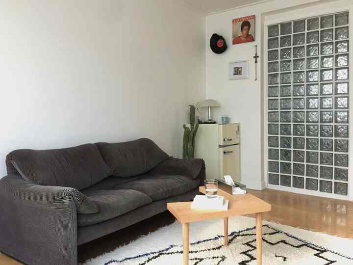 白い壁とガラスブロックのあるコンパクトなリビング、ヴィンテージソファとレトロなミニ冷蔵庫が置かれたミニマルなインテリア空間