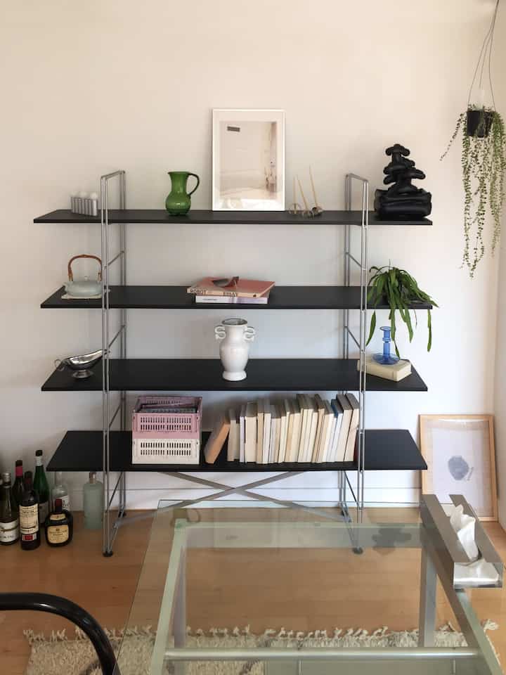 ホワイトの壁とブラックの棚があるナチュラルな色調のリビング、花瓶や本、植物が整然と配置された雰囲気のあるインテリア