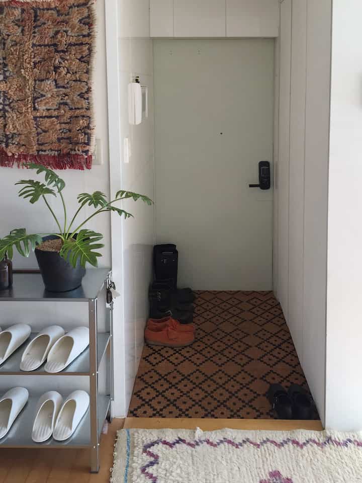 白い壁と金属製の棚、茶色の模様ラグが配置された印象的な玄関インテリア