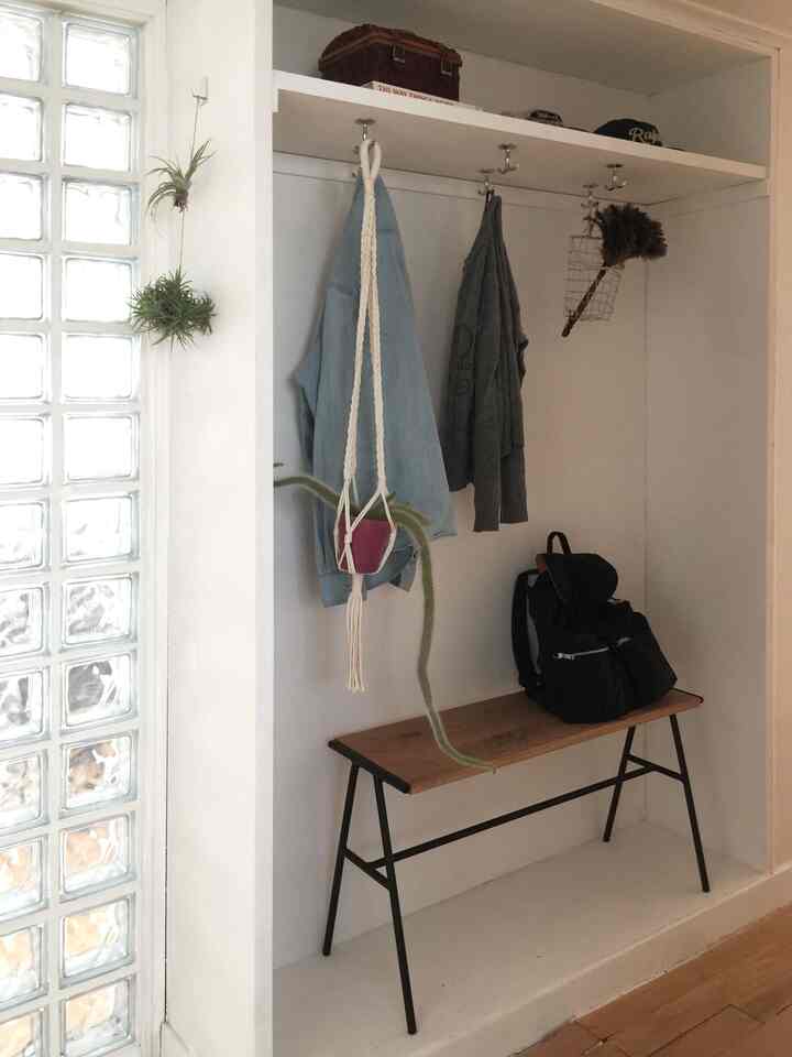 白とナチュラルカラーの玄関クローゼット、木製ベンチとハンギングプランツが調和した印象的な空間