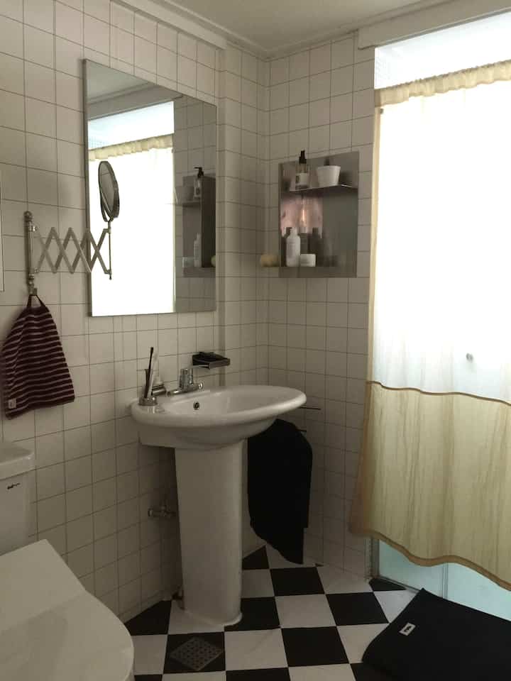 ホワイトタイルの壁と白黒のチェッカーフロアがあるトイレ、洗面台と鏡が配置されたシンプルでヴィンテージな空間