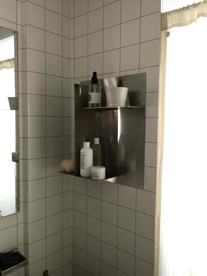 白いタイル壁とステンレス製の棚があるバスルームコーナー、清潔に配置されたバス用品のある雰囲気のあるインテリア