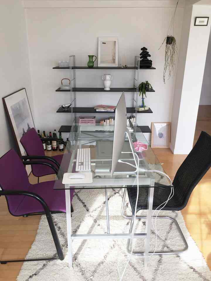 明るい木目調の床と白い壁に配置されたガラステーブルのあるシンプルなホームオフィス空間、パープルの椅子と黒いオフィスチェアが調和している