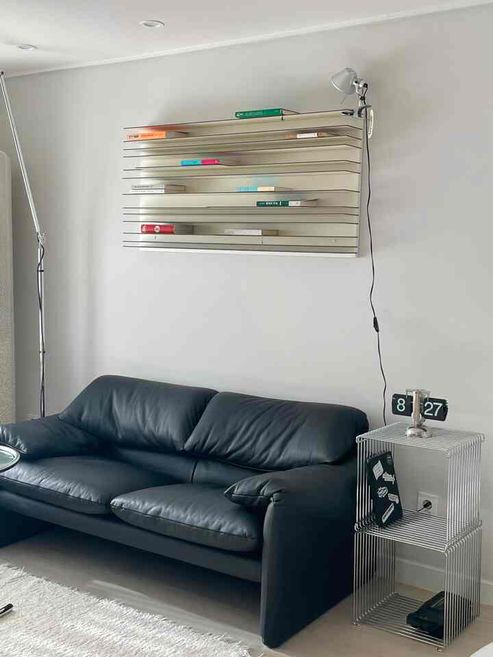 白い壁面とモダンな黒いレザーソファが配置されたシンプルで洗練されたリビングルーム、中央上部にスペクトラムの棚と時計がある空間