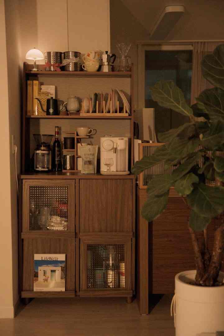 暖かみのある木目調のキャビネットが配置されたおうちカフェ空間、コーヒー器具と大きな緑の植物がある落ち着いたインテリア
