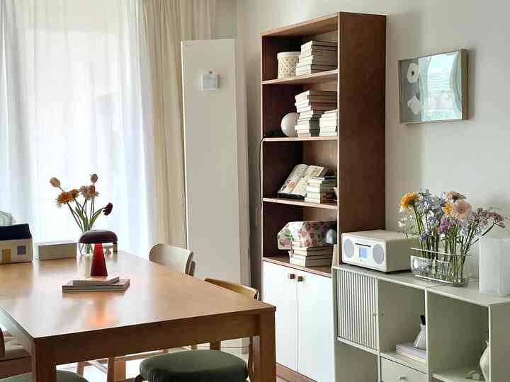 自然光あふれるリビング、木製ダイニングテーブルと本棚、リネンカーテンが配置された落ち着いた雰囲気のインテリア