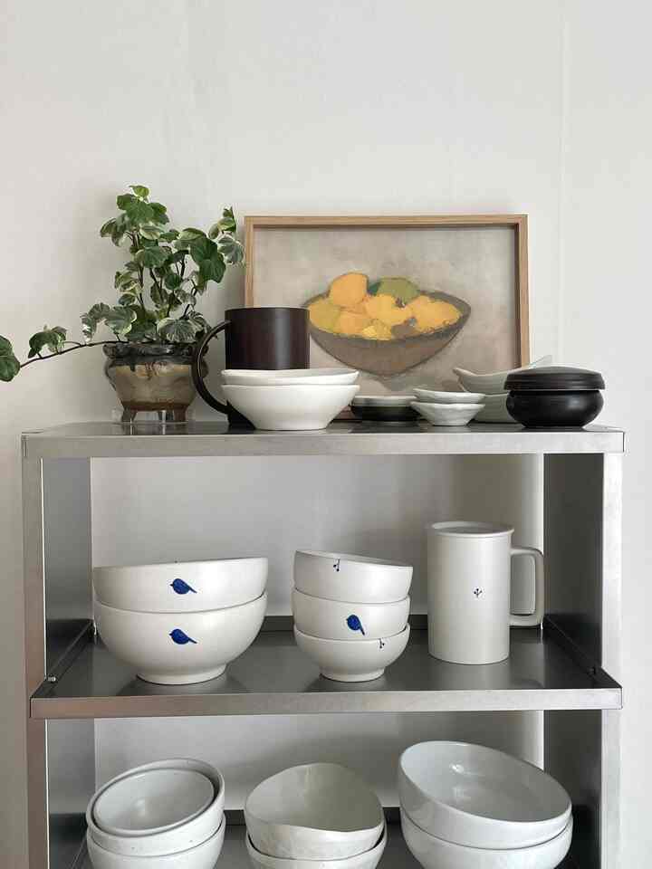 白を基調としたトーンのダイニング空間。ステンレスの棚に食器と植物が配置された、ナチュラルでモダンなインテリア
