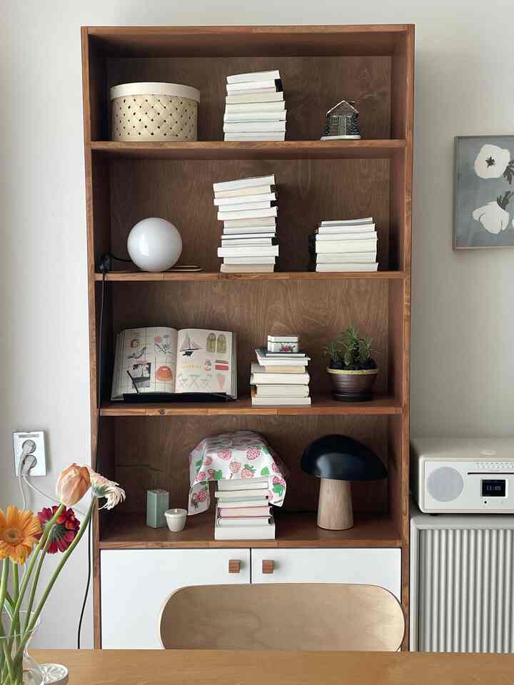 木目調とナチュラルカラーが調和したダイニングルーム、本棚、テーブルランプ、植物が配置された雰囲気のあるインテリア