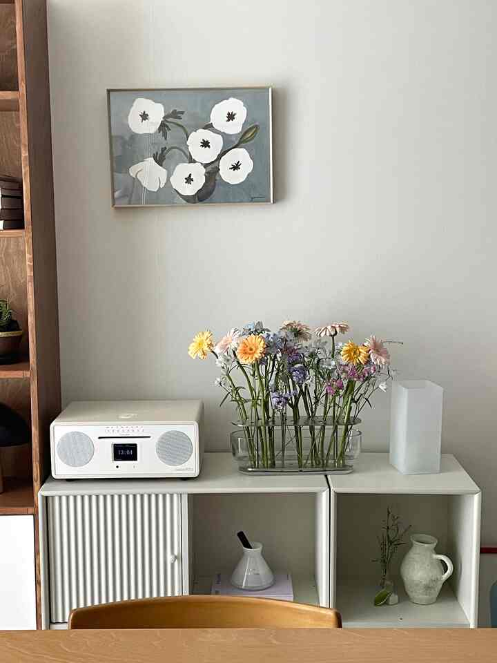 ホワイトとナチュラルカラーが調和するリビング、白いモジュール収納棚の上に花瓶とディフューザーが配置されたシンプルな空間