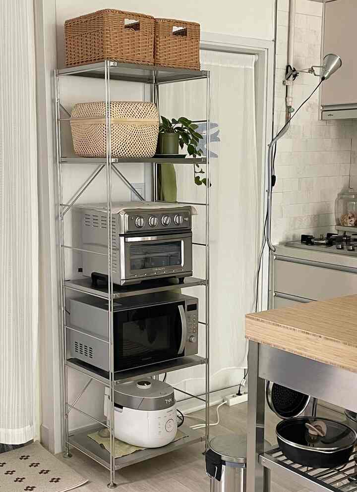 ステンレス棚にオーブン、電子レンジ、炊飯器、ラタンバスケットが配置されたナチュラルモダンなキッチン