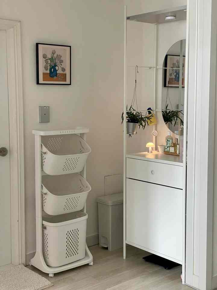 白を基調とした変形間取りの空間、化粧台と収納用のランドリーバスケットが配置された清潔感あるお手洗い