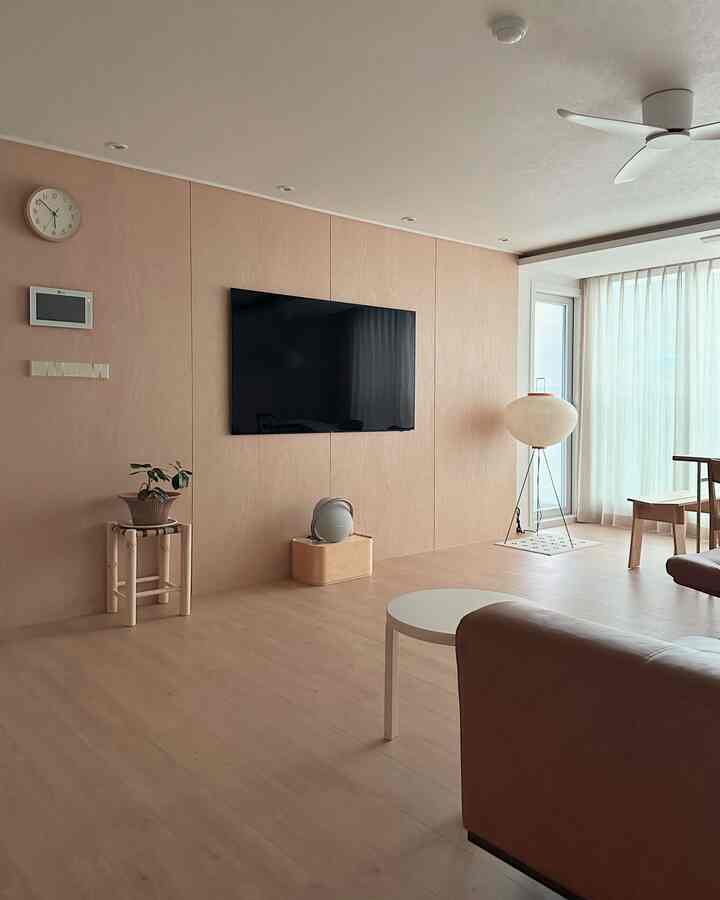 明るくナチュラルカラーのリビング、木製の壁と床、ブラウンのソファと白い丸いコーヒーテーブルが配置されたシンプルな空間