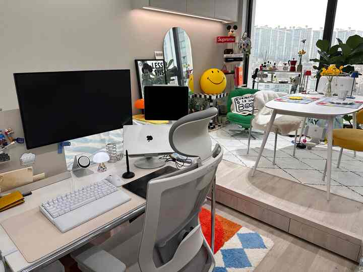 明るいトーンのホームオフィス、モニターアーム付きの広いデスク、カラフルなラグとダイニングテーブルが配置されたモダンで雰囲気のあるインテリア