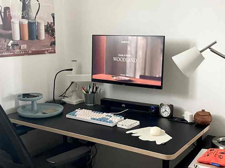 ブラックとスカイブルーのトーンのデスク空間、モニター、キーボード、時計が配置された清潔感のある作業スペース