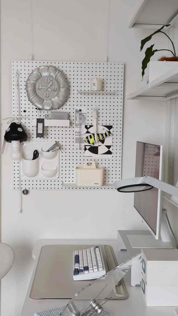 白とグレーのトーンが調和したシンプルなホームオフィス、ペグボードとモニターが配置された清潔感のあるデスクインテリア