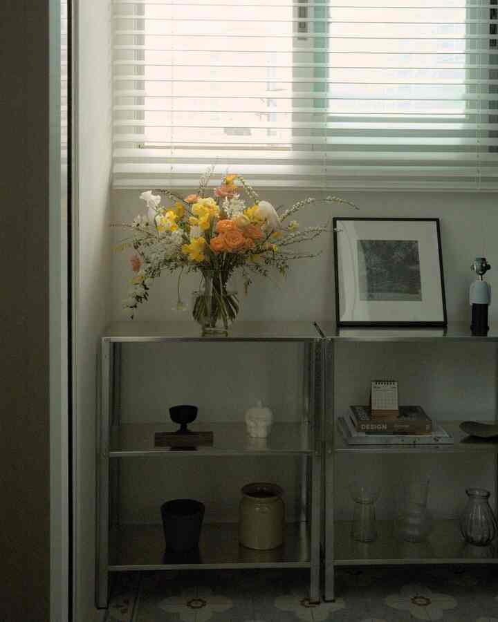 白とシルバーのトーンのリビング、棚に花瓶とオブジェが配置されたミニマルなインテリア