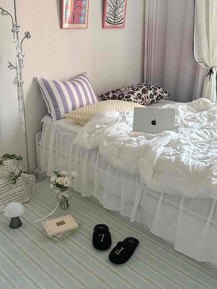 白とナチュラルな色調の寝室、フリル付きベッドスカートと柄の枕が配置された雰囲気のあるインテリア