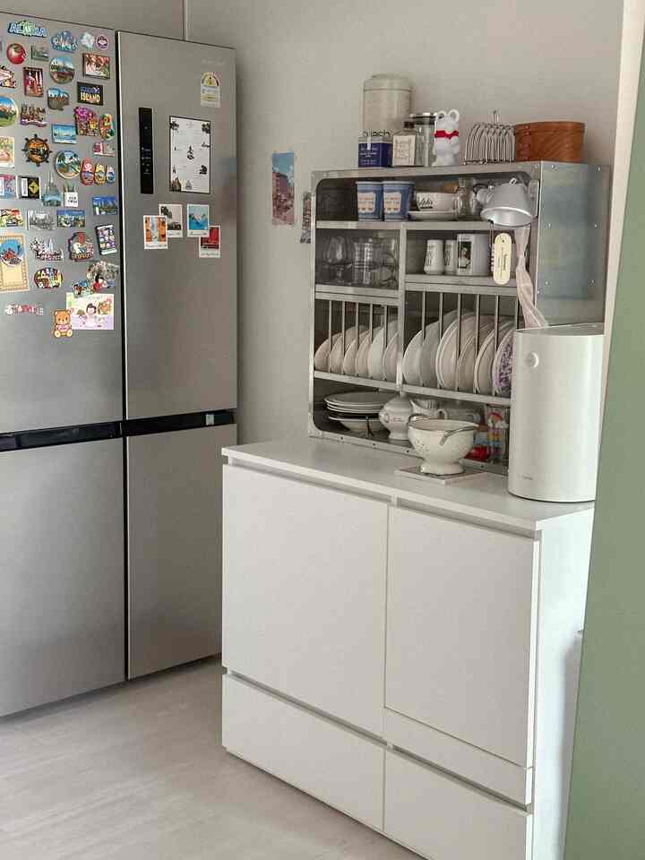 ホワイトトーンのキッチン、冷蔵庫と収納棚に電子レンジと食器が整然と配置された、清潔で実用的な空間