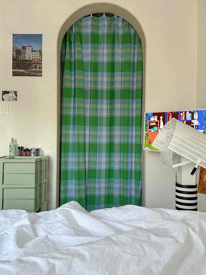 白色の寝具と緑と青のチェック柄カーテンがアーチ型の入口を覆う寝室内のウォークインクローゼット