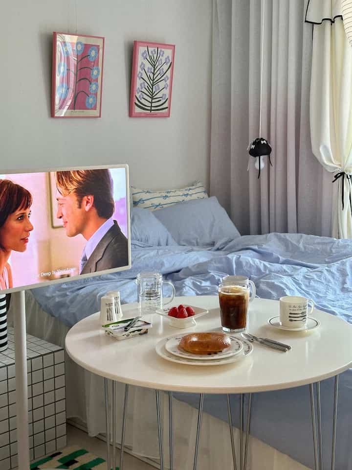 ホワイトとブルーのトーンのワンルーム寝室、ベッドと丸テーブル、テレビ台が配置された雰囲気のあるインテリア