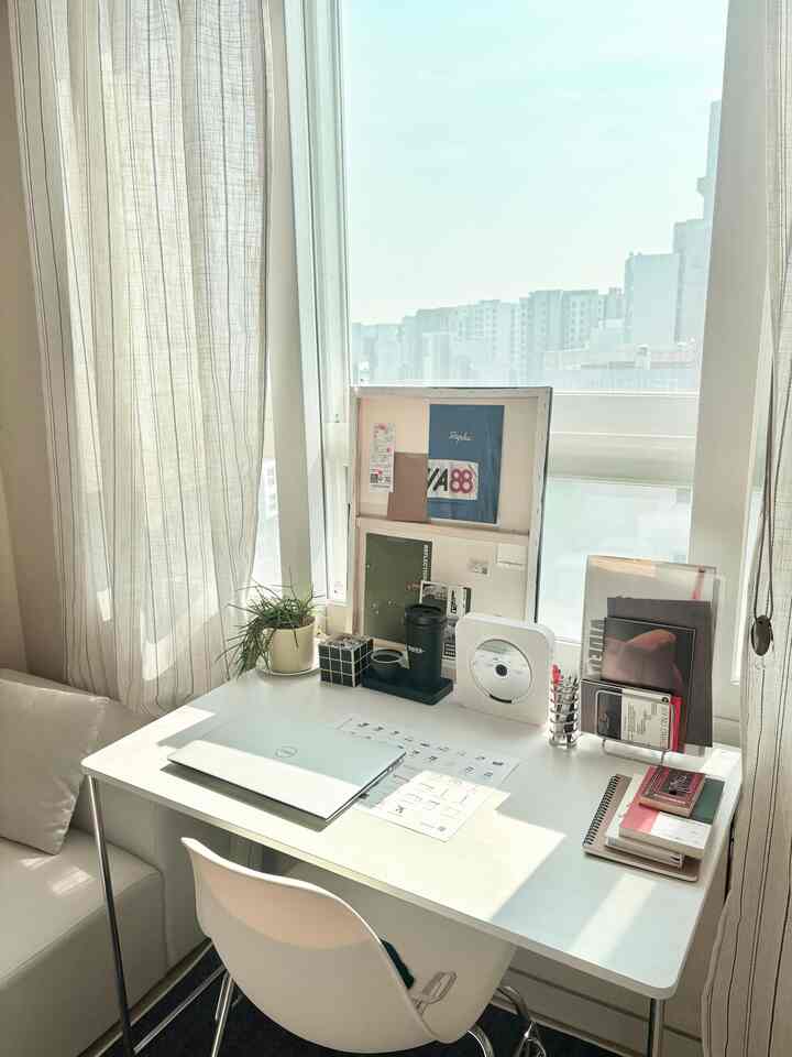 明るいホワイト調のホームオフィス、窓際に置かれたデスクとすっきりしたソファが配置された居心地の良い作業空間