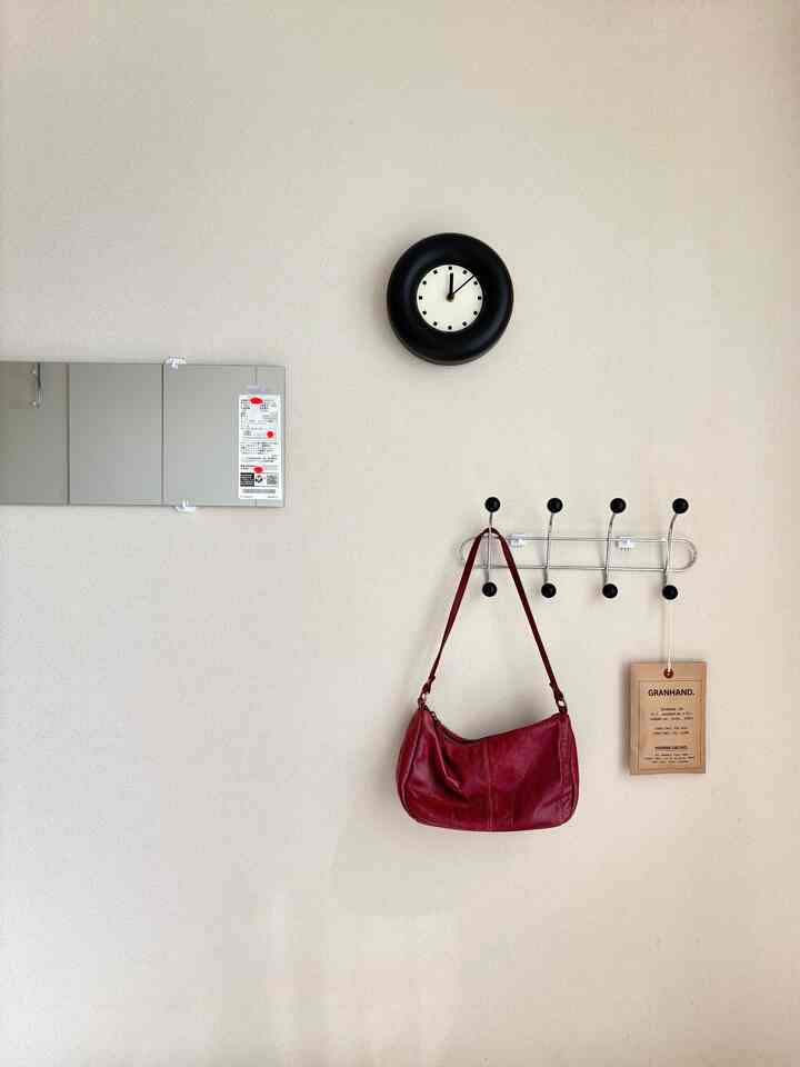 淡いベージュの壁に黒い時計、長方形の鏡、そして赤いバッグが掛けられた玄関の印象的な空間