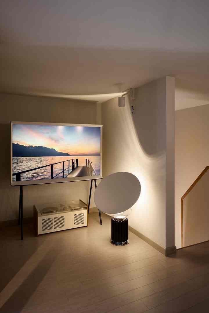 ライトブラウンの木製床とモダンな玄関、テレビスタンド上のサムスン ザ・セリフテレビ、印象的なテーブルランプが配置された雰囲気ある空間